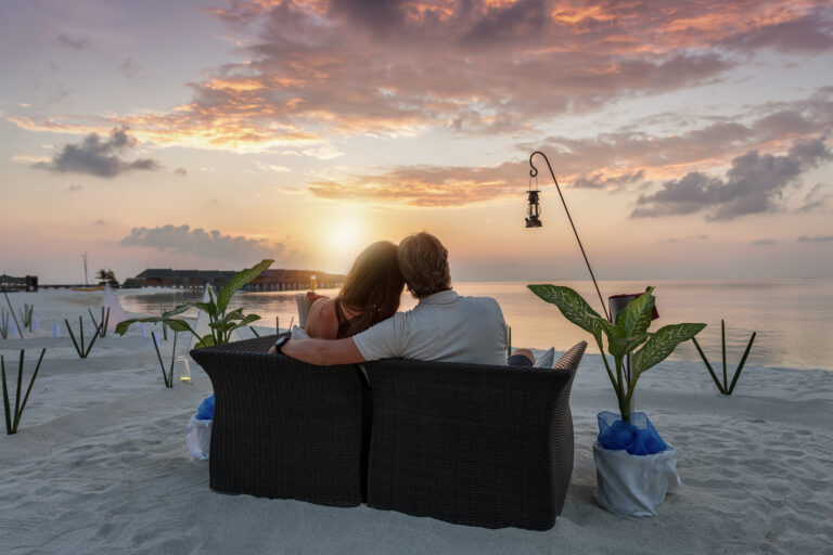 rear-view-couple-sitting-sofa-beach-sunset